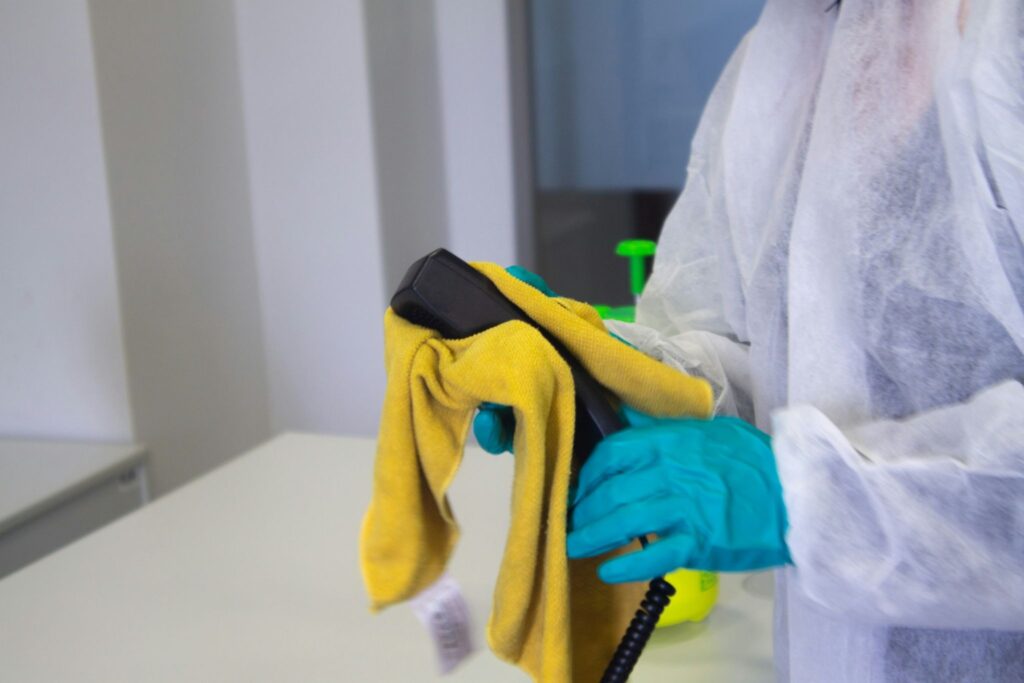 Picture of a person in a white protective suit and blue gloves wiping equipment with a yellow cloth