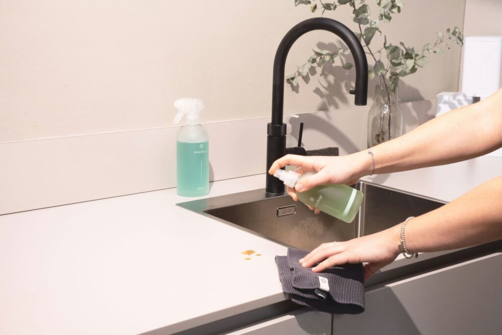 Picture of a person using a green spray bottle and cloth to clean a kitchen counter