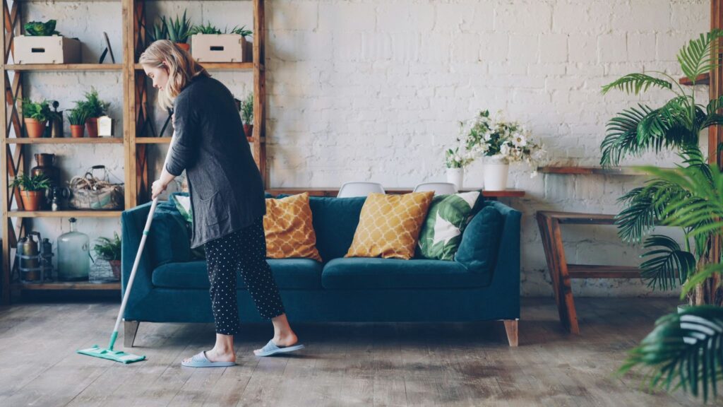 Picture of a woman mopping a hardwood floor in a living room with a blue sofa