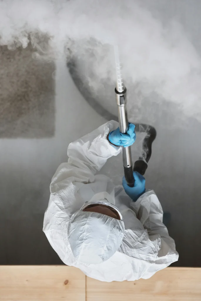 picture of a cleaner from an overhead view wearing a white protective suit and using a steam cleaning wand