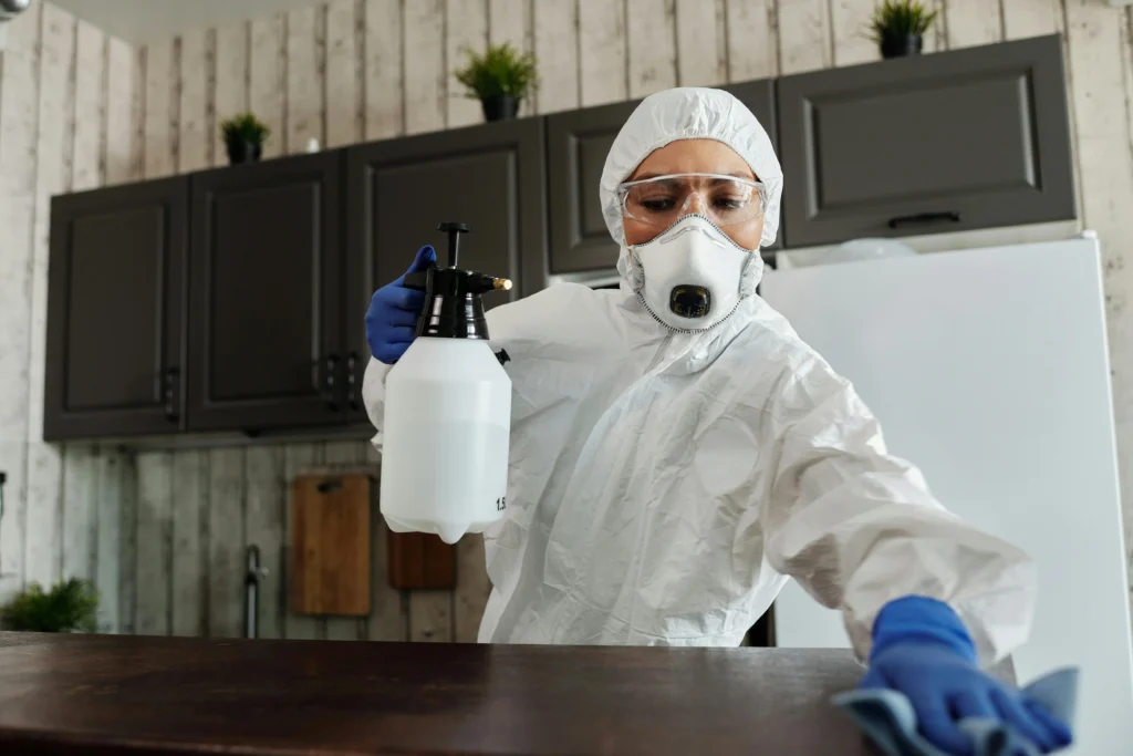 picture of a cleaner in a protective suit and mask using a white pump sprayer on a kitchen counter