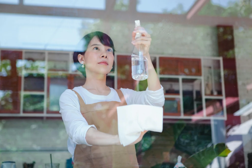 picture of a female cleaner in a brown apron wiping a glass window viewed from the outside looking indoors
