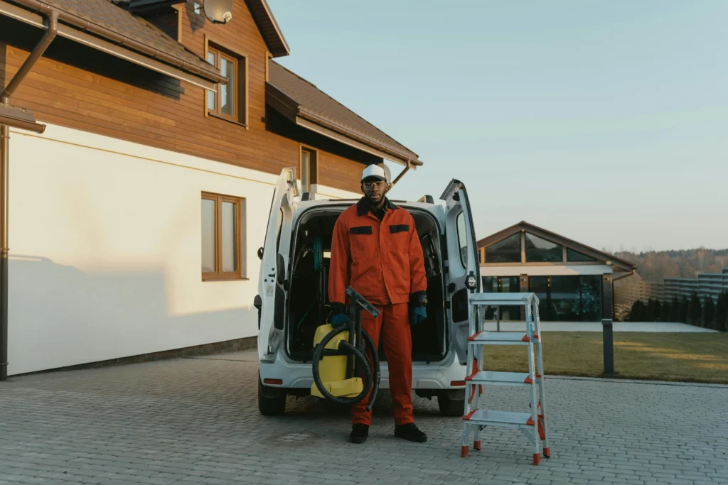 picture of a male cleaner in an orange uniform holding a yellow vacuum cleaner in front of an open white van