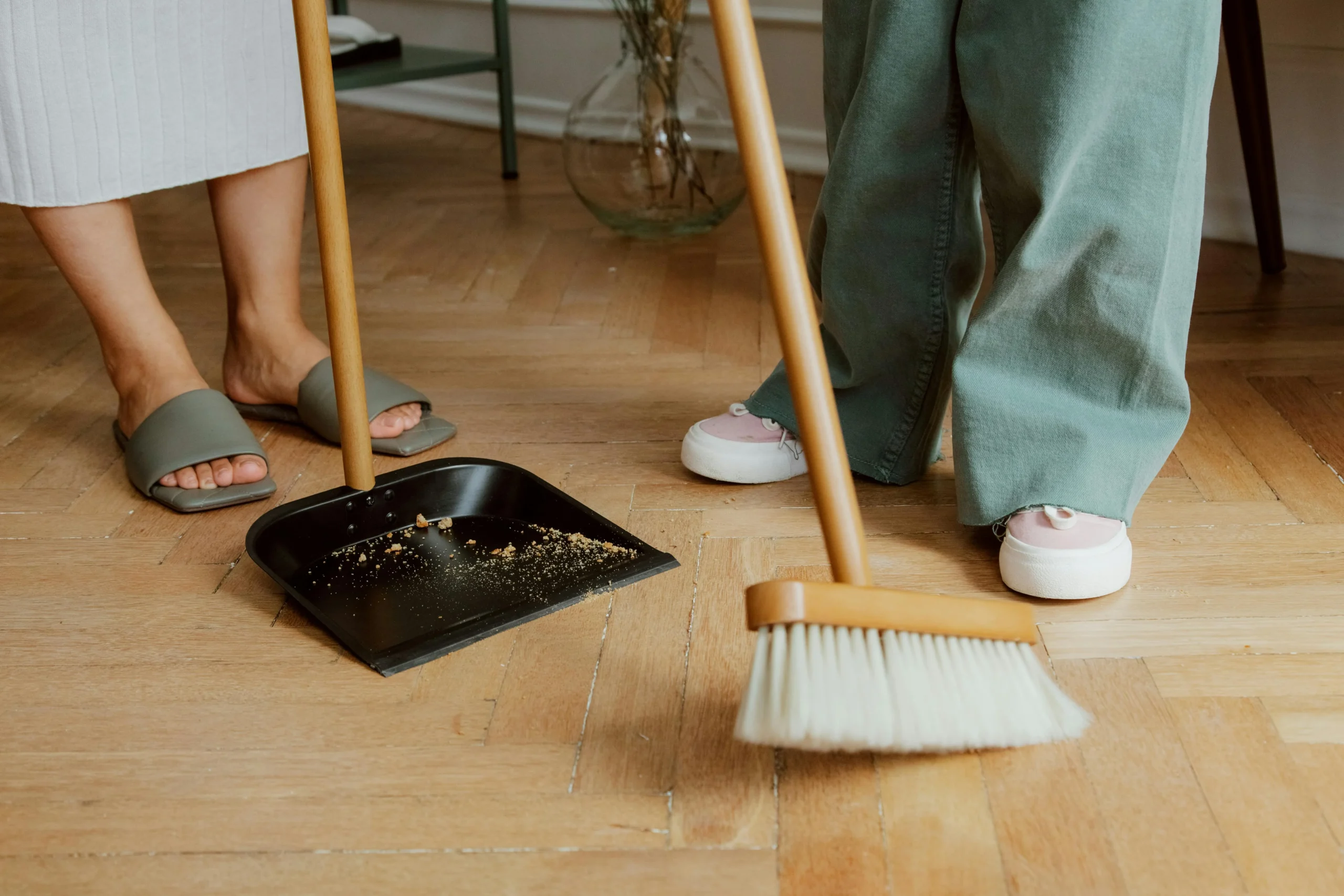 Person sweeping dirt into a dustpan on a parquet floor