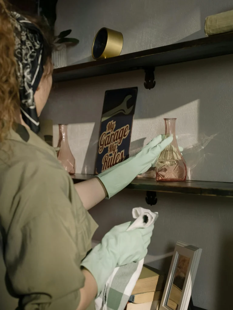 picture-of-a-person-wearing-light-green-gloves-using-a-white-cloth-to-carefully-dust-a-wooden-wall-shelf