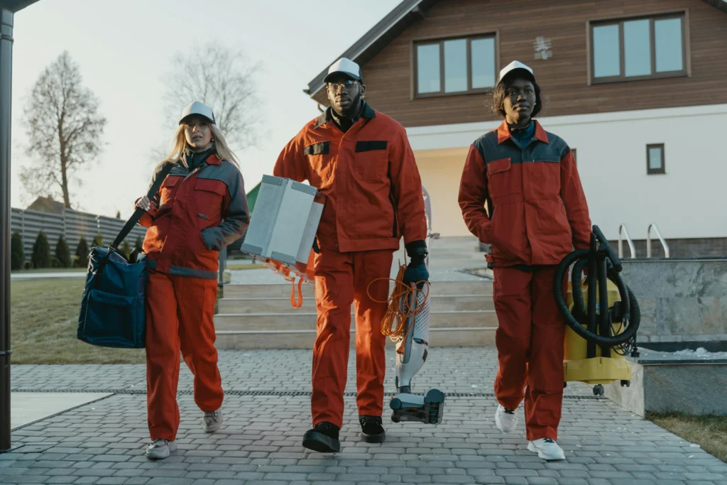 picture of three cleaners in orange uniforms walking down a stone path carrying supplies to perform the best luxury cleaning services london has to offer