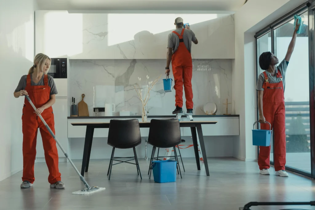 picture of three cleaners in orange uniforms working in a modern kitchen with one on a stepladder