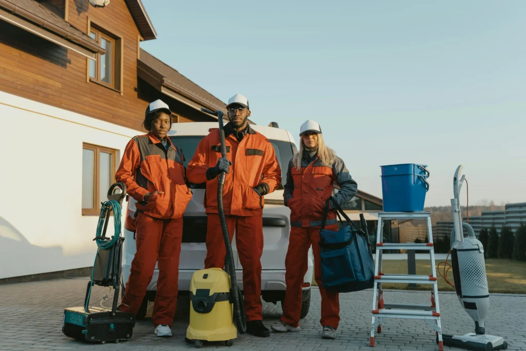 picture of three cleaning specialists in orange uniforms posing with equipment outside a house