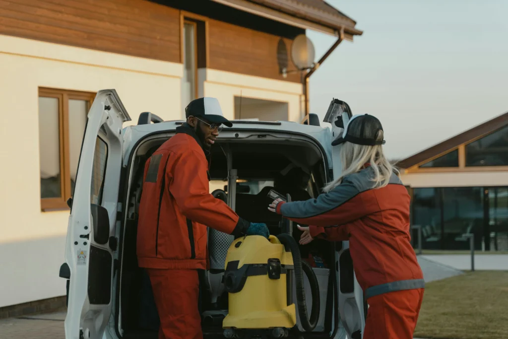 picture of two cleaners in orange uniforms unloading a yellow vacuum from a white van