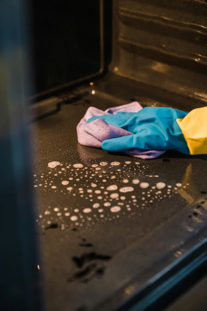 Picture of a gloved hand wiping soapy residue from the glass door of an oven