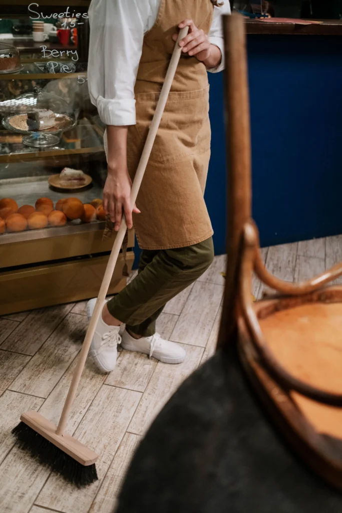Picture of a person in an apron sweeping a cafe floor