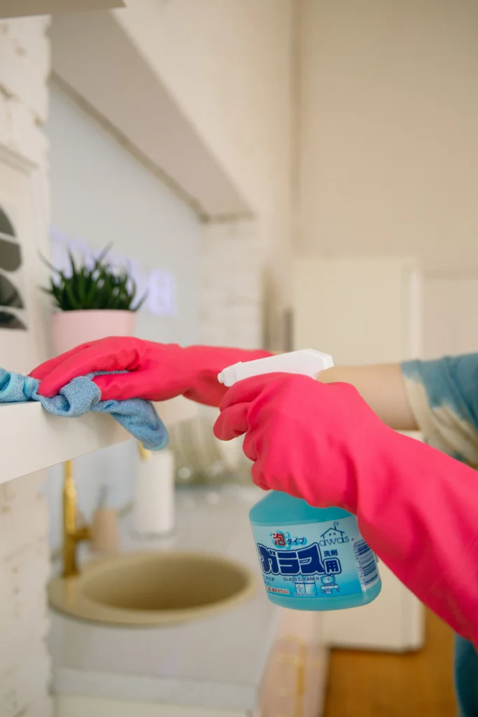 Picture of a person in pink gloves spraying a shelf