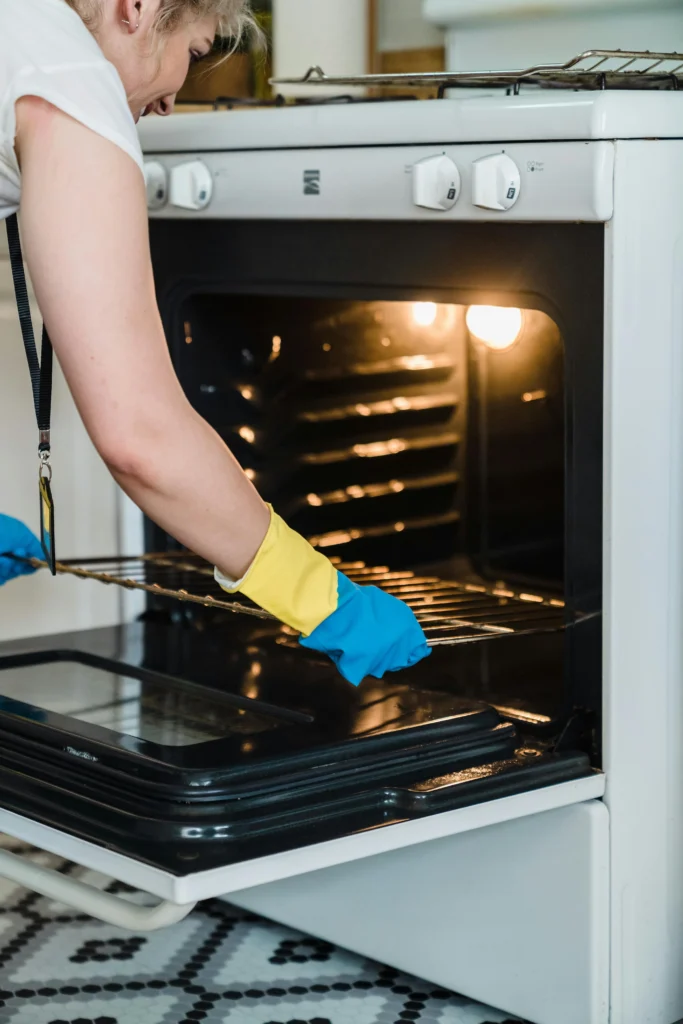 Picture of a person wearing rubber gloves removing a metal rack from a white oven