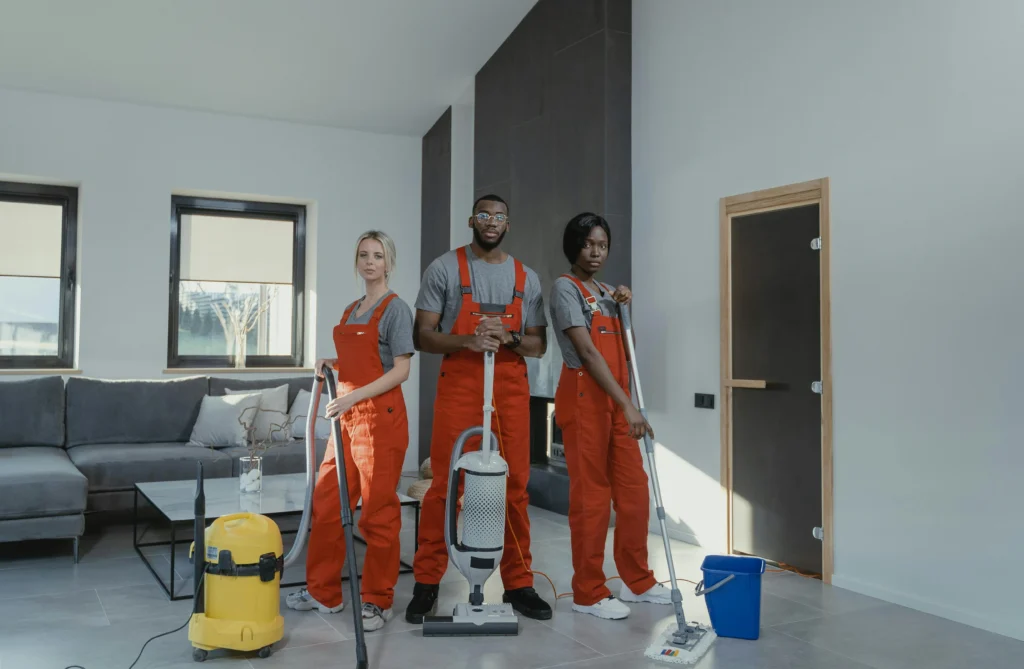 Picture of three professional cleaners in orange uniforms holding cleaning equipment in a modern home