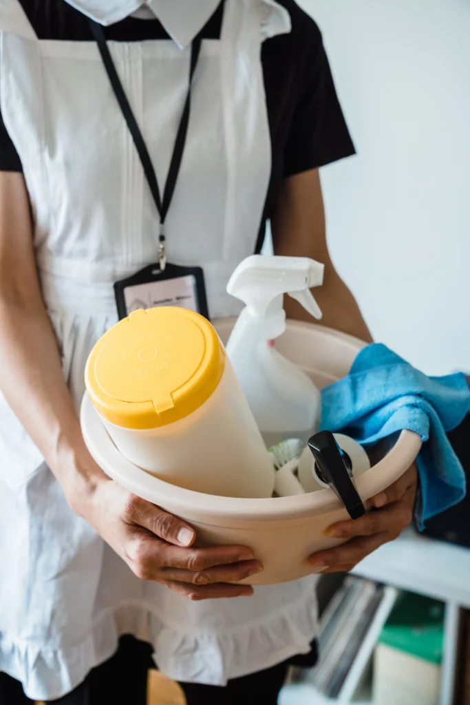 Picture of a cleaner holding a basin full of cleaning supplies