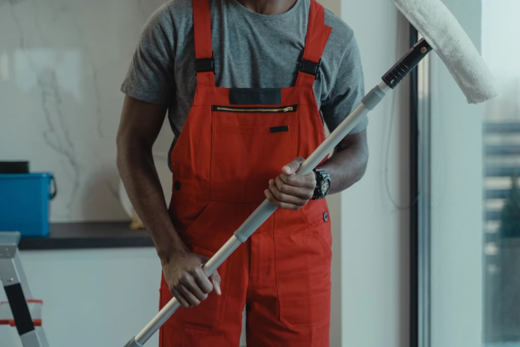 Picture of a cleaner in red overalls holding a long duster